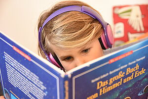 Ein Kind liest in einem Heft und hört dazu den passenden Hörtext
